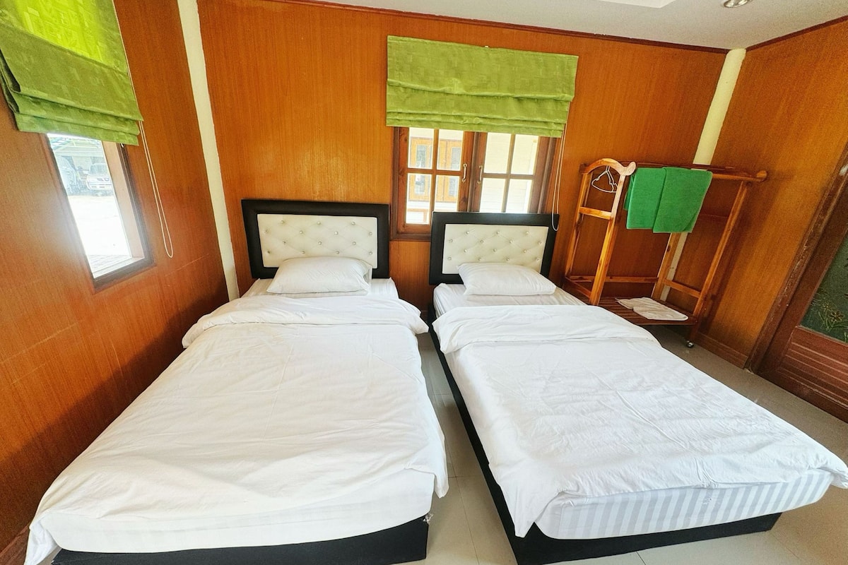 A double room with two beds, wooden walls, a window with a view, and a green towel rack.