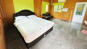 A hotel room with a large bed, a wooden headboard, a bench, a small table, and a window with curtains. - OYO 75497 Uncle Odd Talay View Resort (Nakhon Nayok)