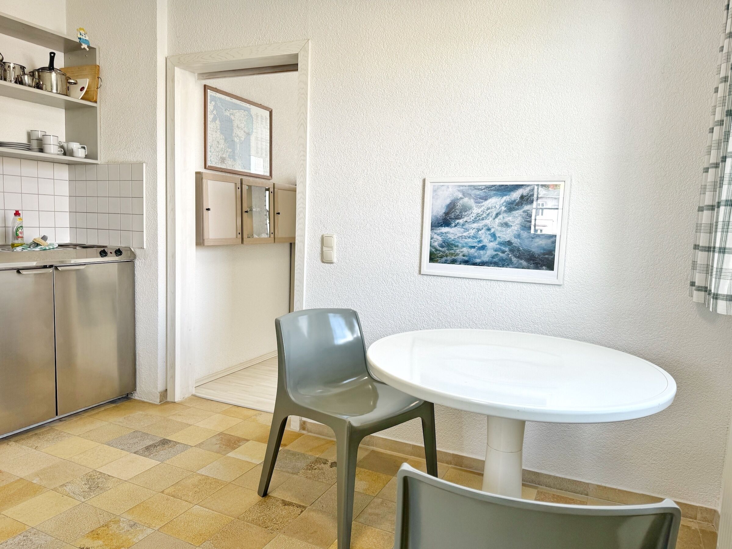 Cozinha compacta com área de jantar, destacando uma mesa redonda e duas cadeiras, uma geladeira e um painel de azulejos.