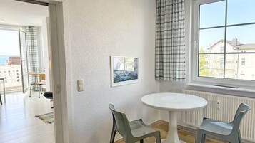 Ein Zimmer mit einem weißen runden Tisch, zwei grauen Stühlen, einem Fenster mit Blick auf Gebäude und einer Tür zu einem anderen Raum.