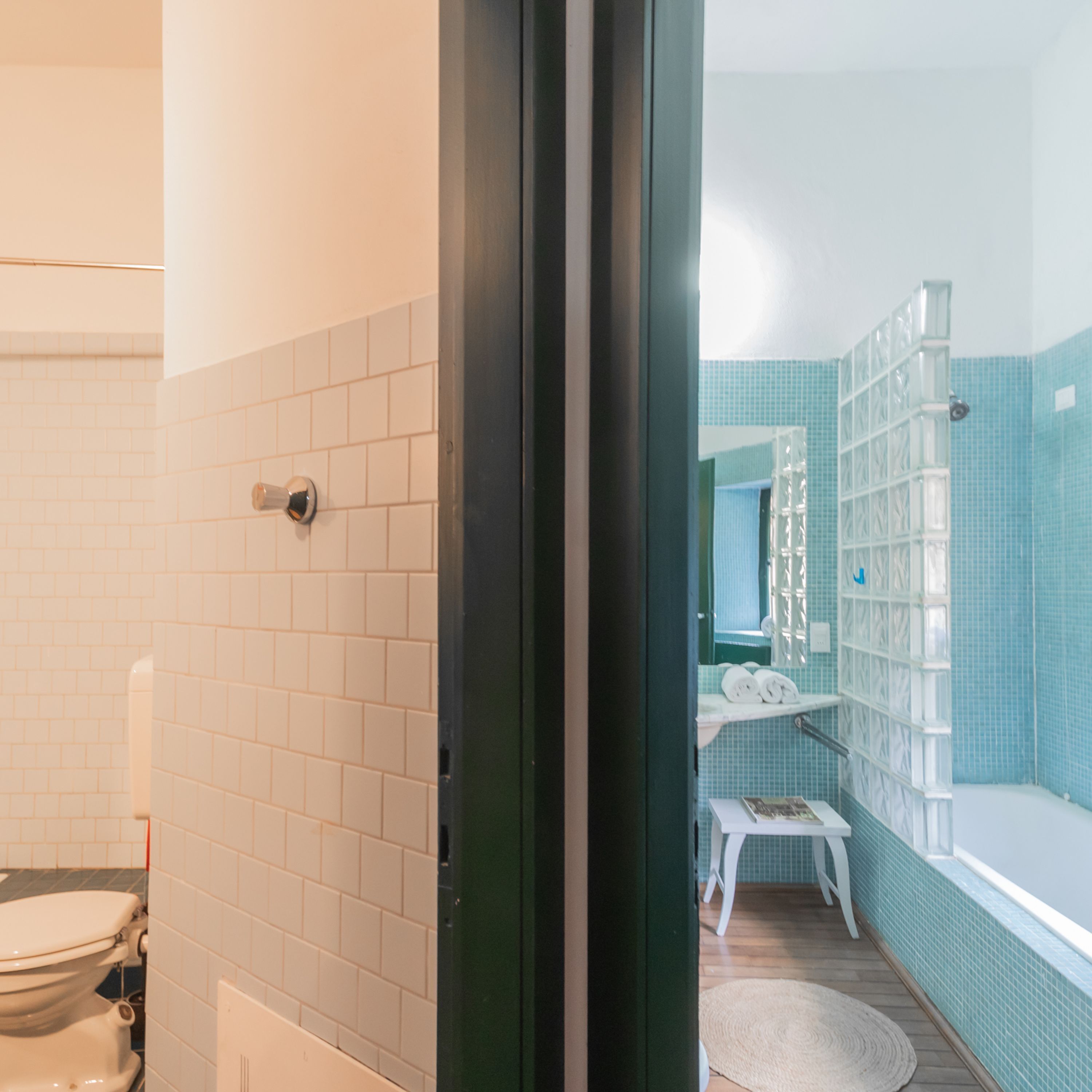 A bathroom with white tiled walls, a toilet, a shower area with a glass enclosure, and a small white stool.