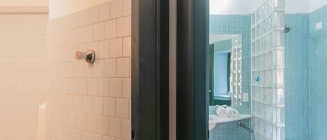 A bathroom with white tiled walls, a toilet, a shower area with a glass enclosure, and a small white stool.
