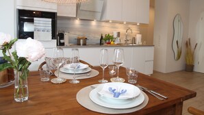 A modern kitchen with white cabinets, a wooden dining table set for a meal, and a hanging light fixture. - Hundefreundliche Neubauwohnung Direkt am Wasser! (Eilsum)