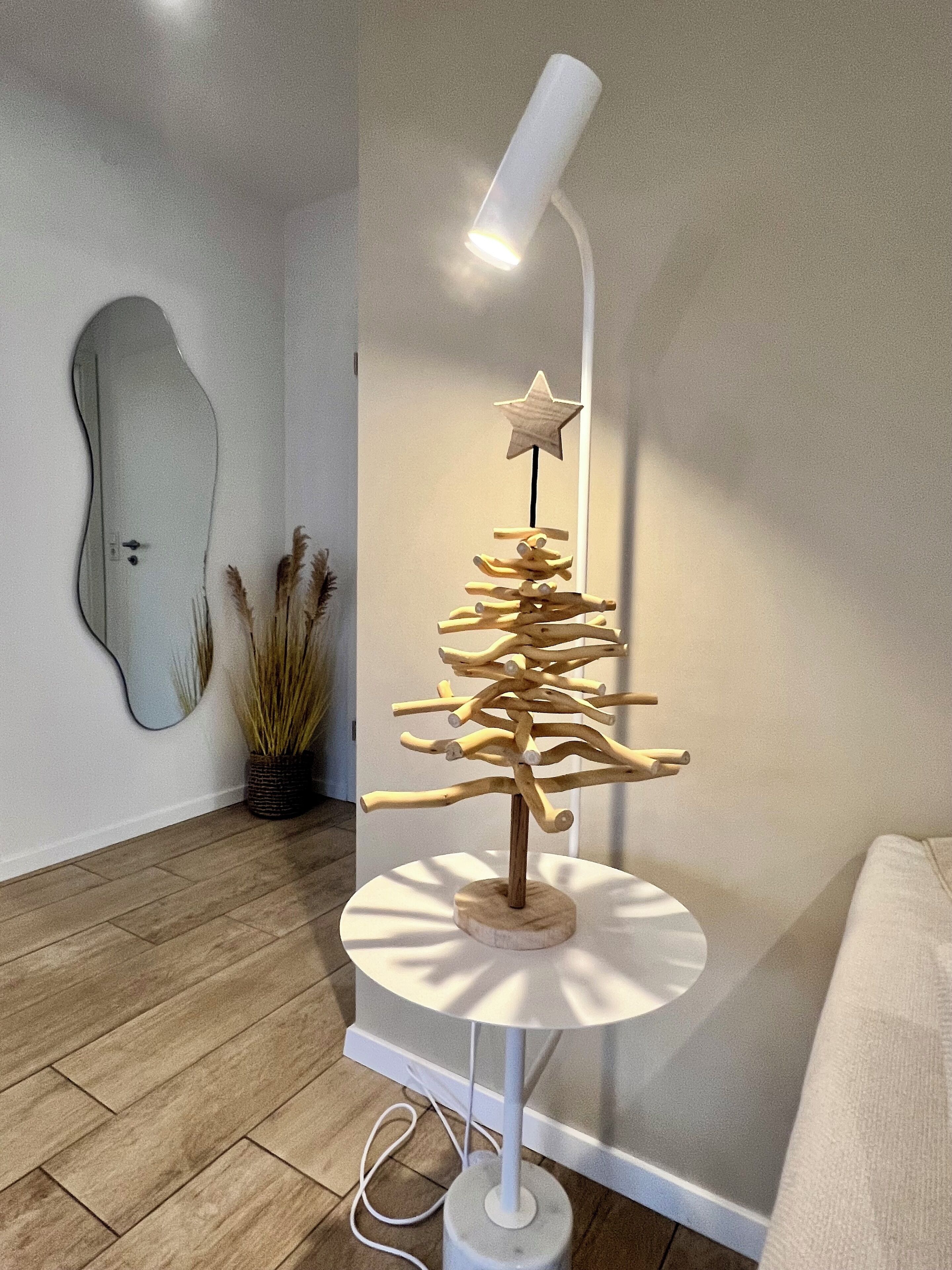 A modern lamp with a unique tree design on a white base, positioned on a wooden floor in a room with a minimalist decor.