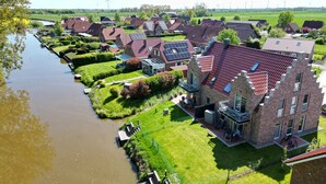 A residential area with houses, a canal, and wind turbines in the background. - Hundefreundliche Neubauwohnung Direkt am Wasser! (Eilsum)