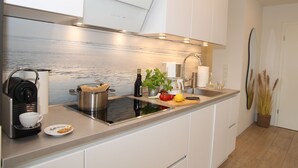 A modern kitchen with a built-in stove, a coffee machine, a sink, and a countertop with various kitchen items. - Hundefreundliche Neubauwohnung Direkt am Wasser! (Eilsum)