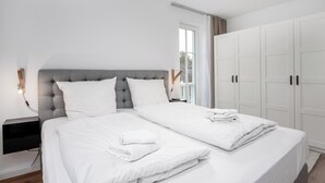 Camera da letto moderna con un letto grande, biancheria bianca, una testiera imbottita grigia e un armadio con maniglie nere.
