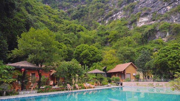 A swimming pool with lounge chairs, surrounded by lush greenery and a mountain backdrop. - Tràng An Hometown Homestay (Ninh Binh)