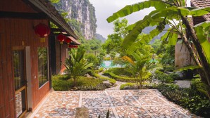 A courtyard with a tiled floor, surrounded by lush greenery and a mountain backdrop. - Tràng An Hometown Homestay (Ninh Binh)