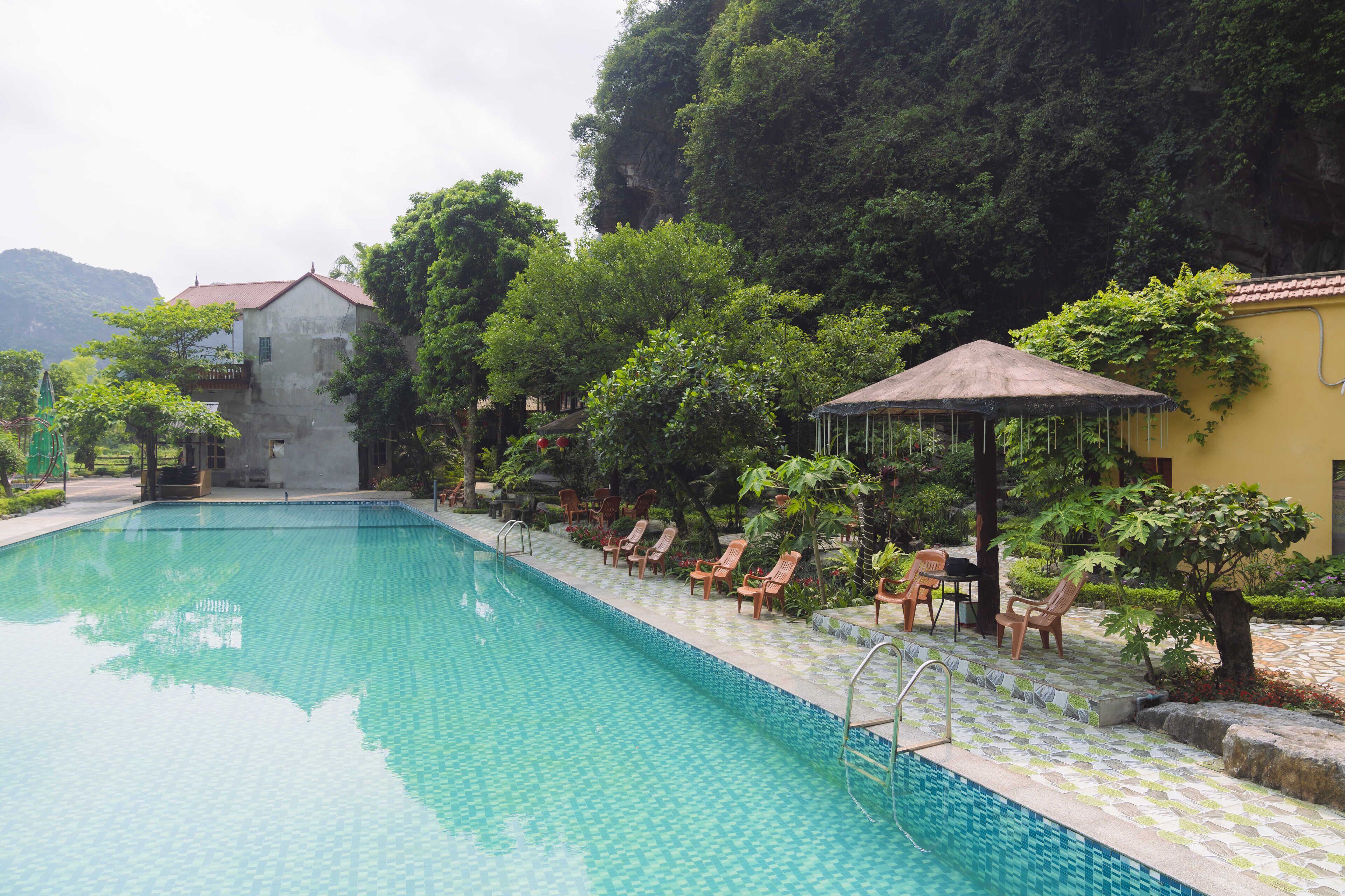 Piscina com espreguiçadeiras e um gazebo, rodeada por vegetação exuberante e um pano de fundo montanhoso.