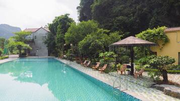 Piscina com espreguiçadeiras e um gazebo, rodeada por vegetação exuberante e um pano de fundo montanhoso.