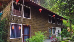 A traditional brick building with multiple windows and doors, surrounded by lush greenery and a tiled pathway. - Tràng An Hometown Homestay (Ninh Binh)