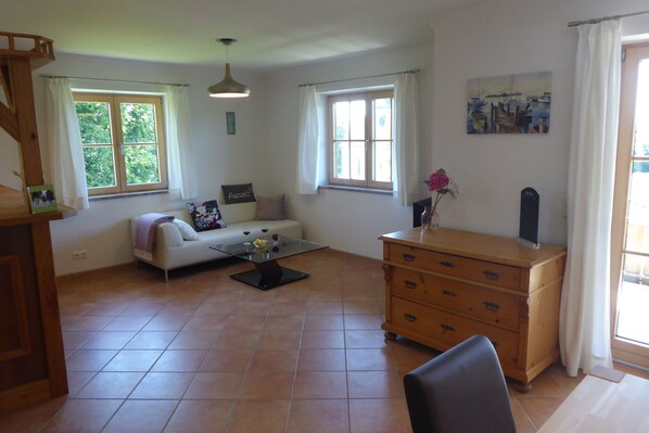 Ein geräumiges Wohnzimmer mit einer Couch, einem Couchtisch, einer Holzkommode und großen Fenstern.