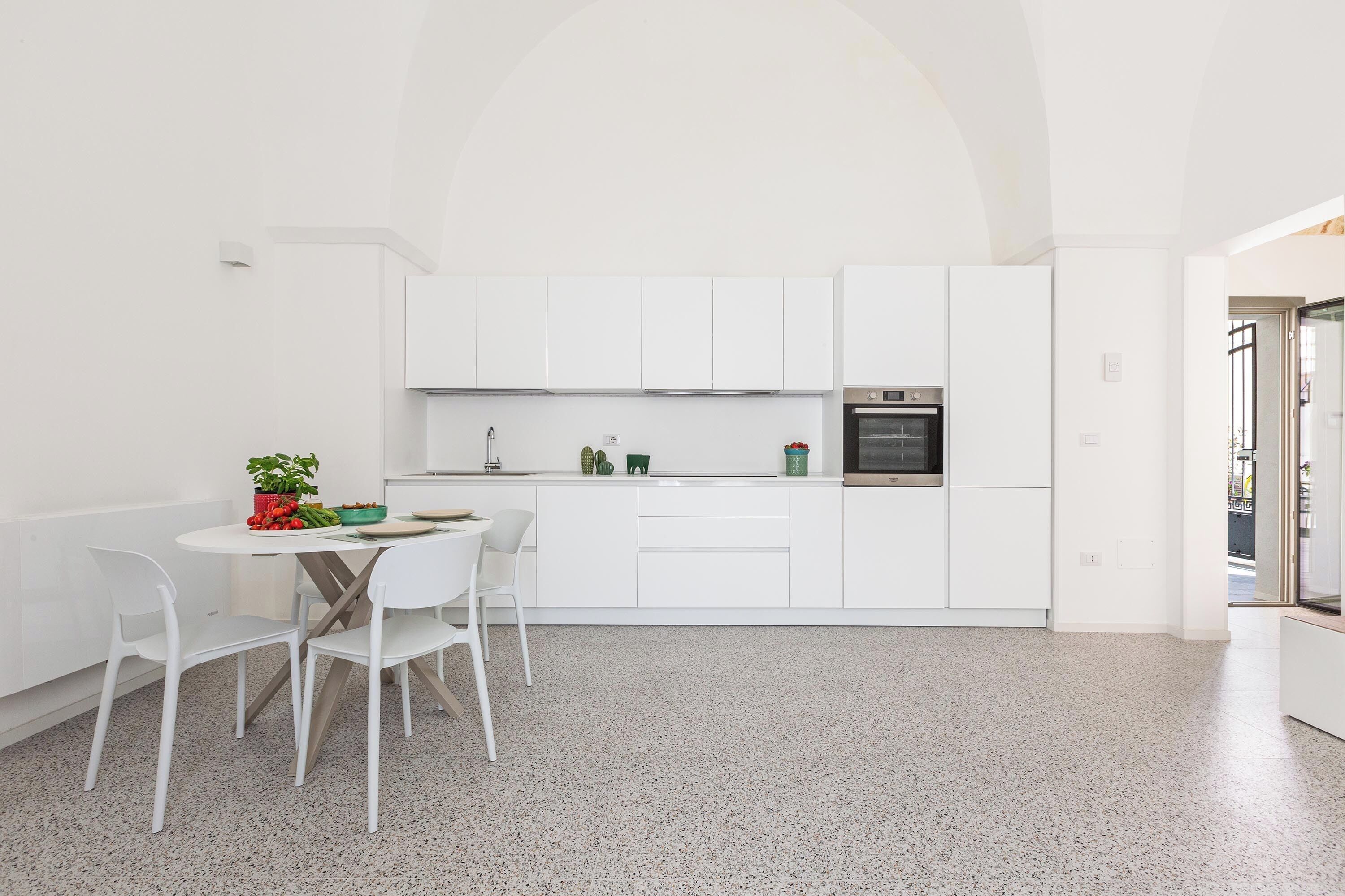 A modern kitchen with white cabinetry, a stainless steel oven, and a dining area with a white table and chairs.