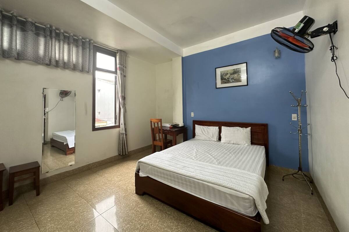 A bedroom with a bed, a desk, a chair, a standing lamp, and a coat rack.
