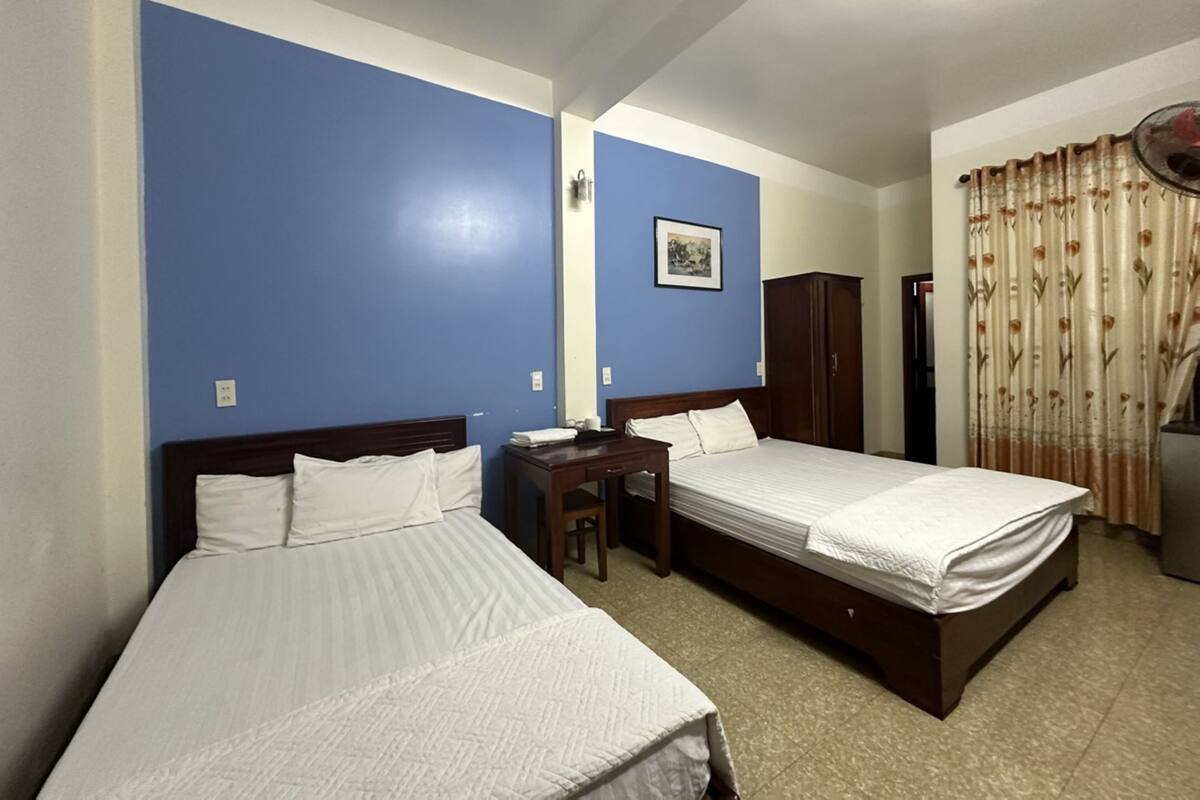 A hotel room with two single beds, a small desk, a wardrobe, and a mirror on the wall.