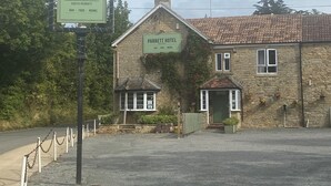 Un edificio de piedra con un letrero que dice "Parrett Hotel", ofreciendo bar, comida y habitaciones.