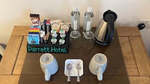 Mesa de Parrett Hotel con una cafetera, cartones de leche, bolsitas de té y una bandeja de bocadillos.