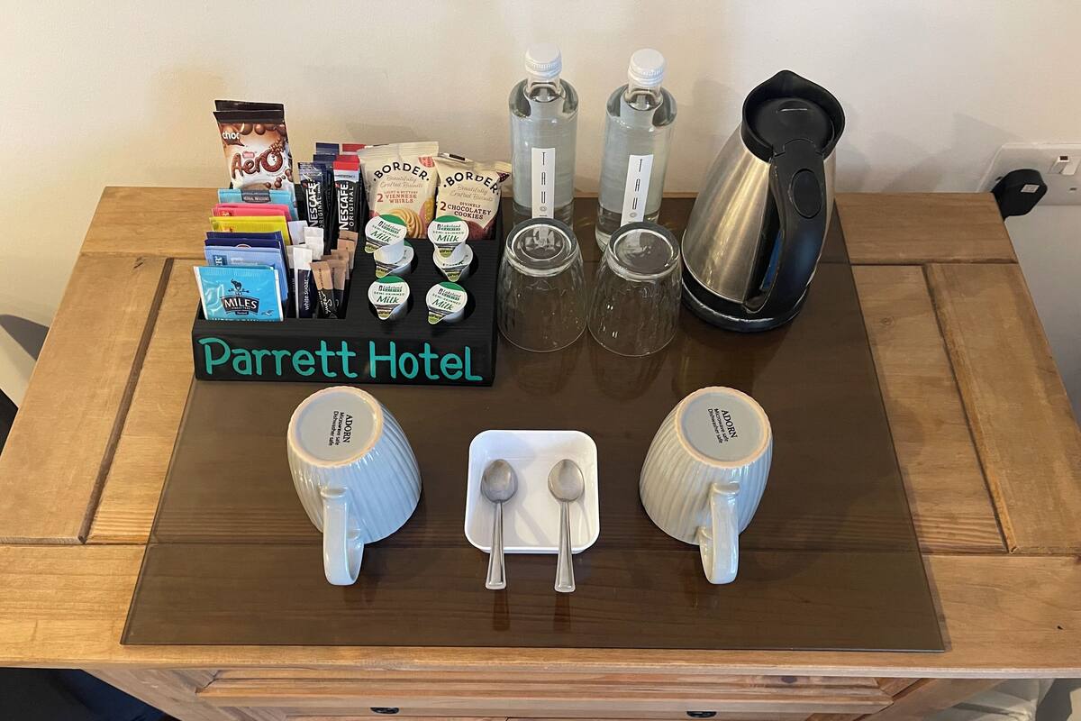 A Parrett Hotel table with a coffee maker, milk cartons, tea bags, and a tray of snacks.