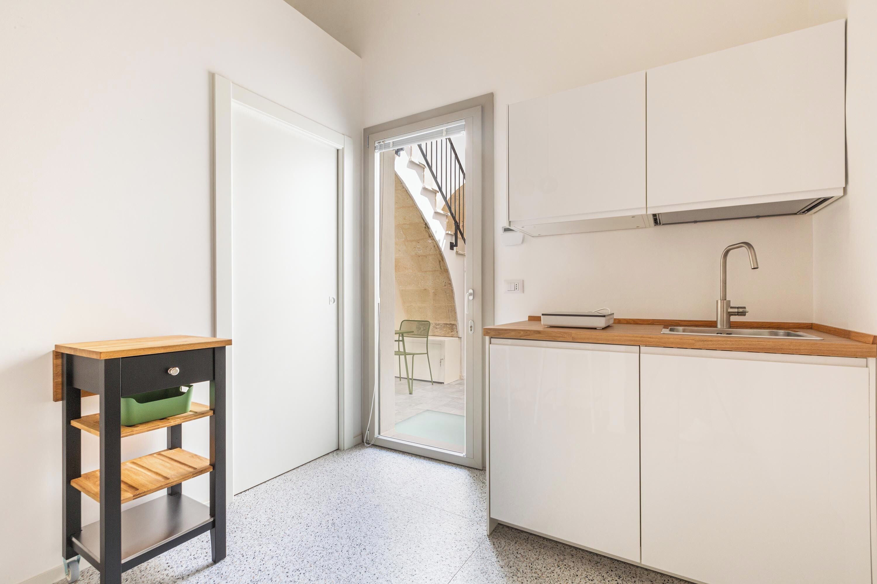 A kitchen with white cabinets, a wooden countertop, and a black metal table with shelves.