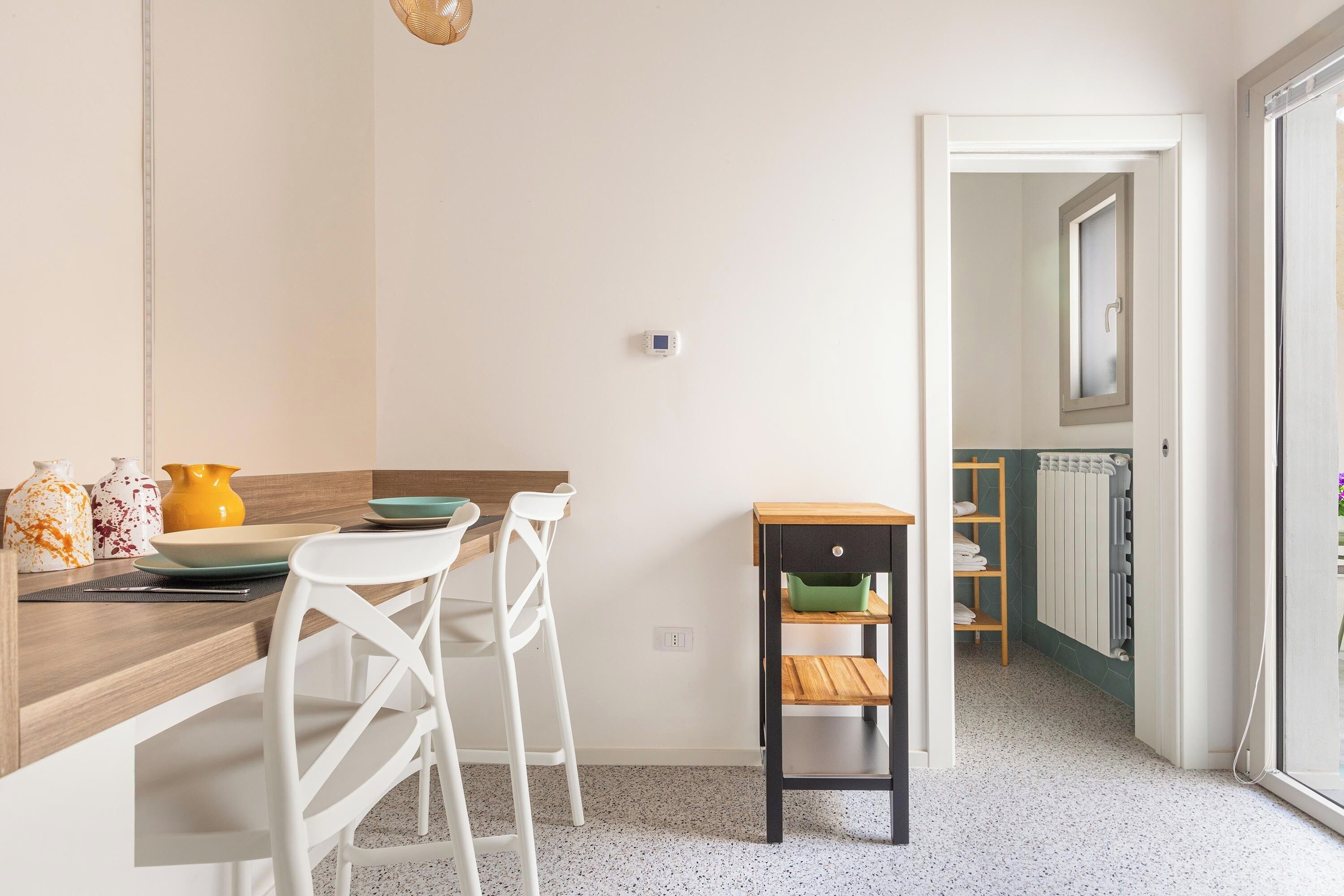 Een moderne keuken met witte stoelen, een houten tafel en een bijzettafeltje met een groene tas.