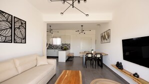 Una sala moderna con un sofá, una mesa de centro de madera y un televisor. Hay un comedor con una mesa y sillas. Se observa una cocina al fondo.