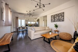 A modern living room with a sofa, coffee table, and dining area. - FN Suites (Santorini)
