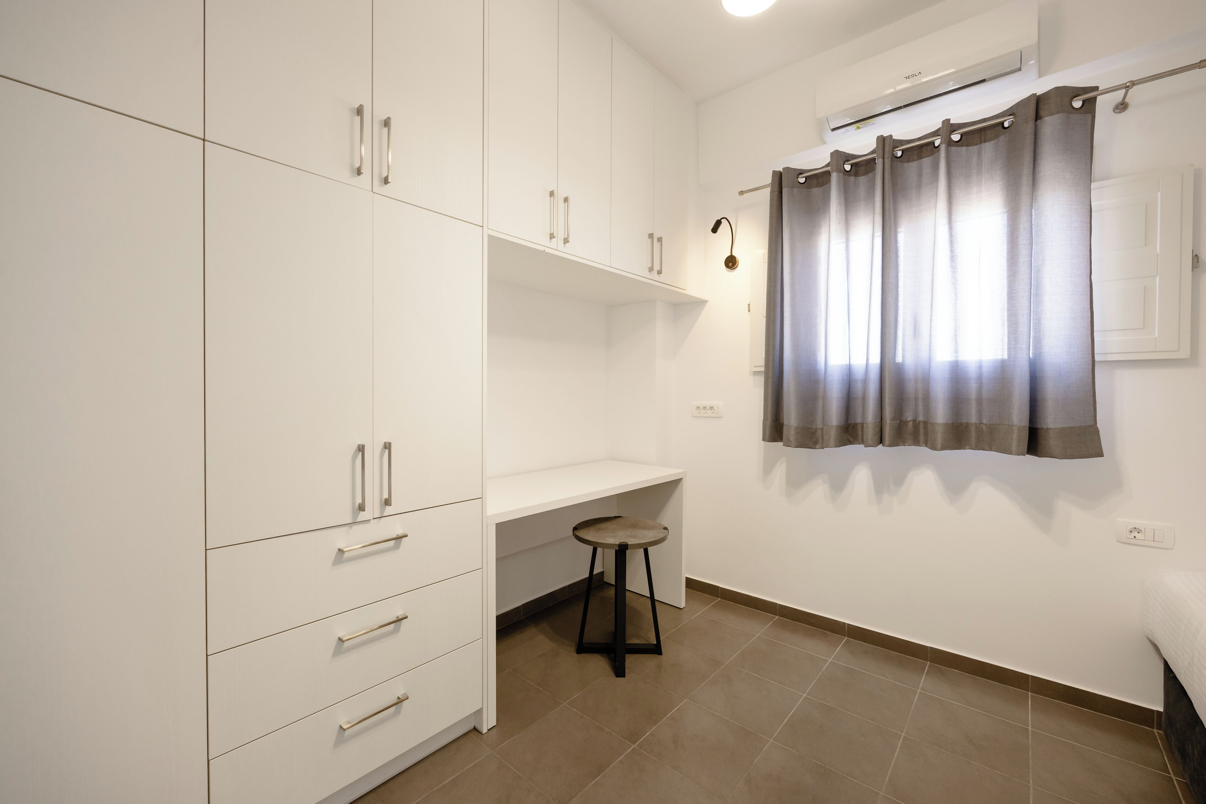 A room with a white wardrobe, a desk, a stool, and a curtain.