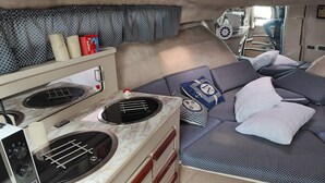 A compact kitchenette with a stove, sink, and microwave. There is a bed with patterned bedding and pillows. - Virginia Bed and Boat (Syracuse)