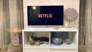 A flat-screen TV mounted on a white entertainment center with a decorative tree and various items on the shelves. - Calm 2P Flat with A/C, Large Terrace, Near Beach and Shops in Central Menton (Menton)
