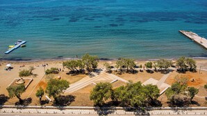 A coastal area with a beach, trees, and a pier extending into the sea. - Directly before the sea.Direkt vor dem Meer (Vouliagmeni)
