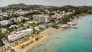 A coastal town with a prominent hotel featuring multiple floors, a beach, and a clear view of the sea. - Directly before the sea.Direkt vor dem Meer (Vouliagmeni)