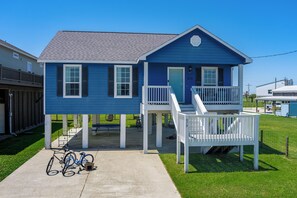 A two-story blue house with a porch, a staircase, and a bicycle parked outside. - Cute 3BR/2Bath with Lift in the heart of Crystal Beach, Texas! (Bolivar Peninsula)
