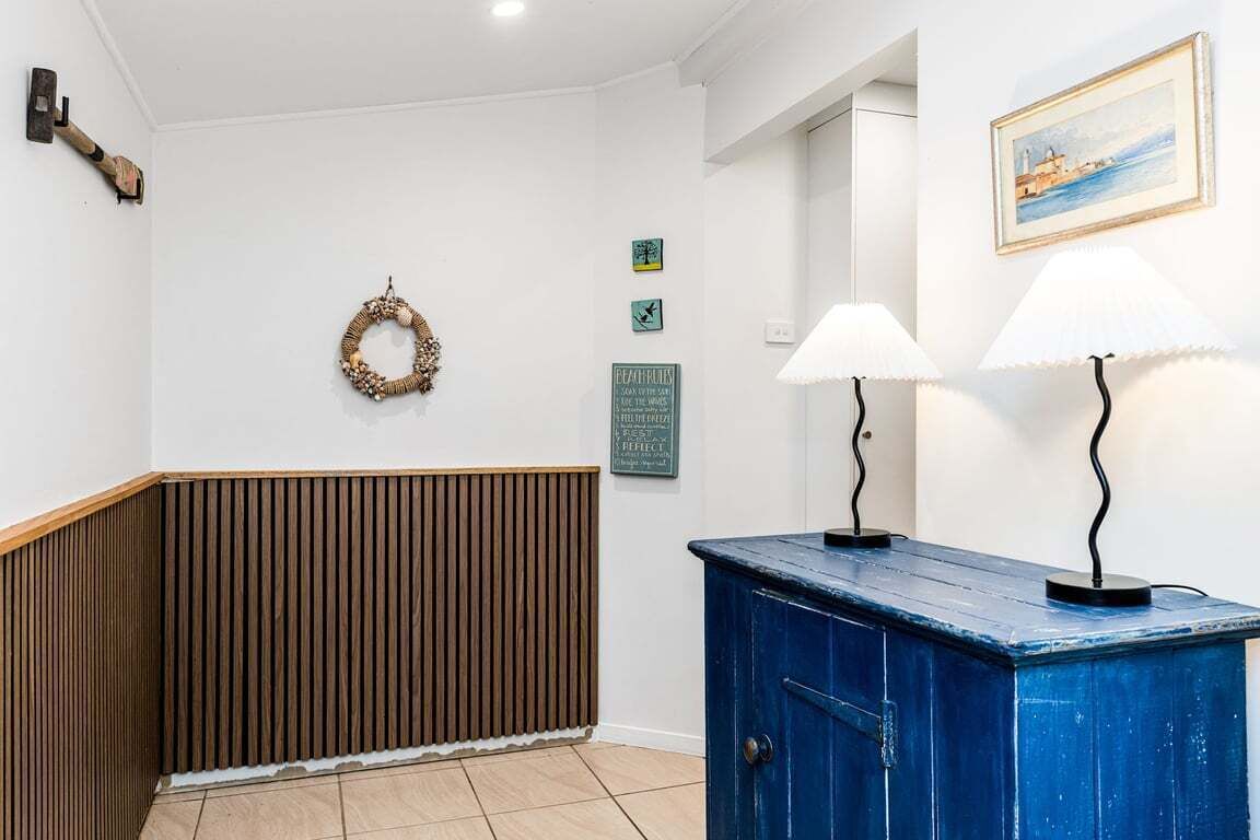 A hallway with a wooden panel wall, a blue cabinet, and wall-mounted lamps.