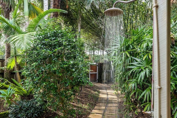 A lush garden with a pathway leading to a shower area surrounded by dense foliage and tropical plants.