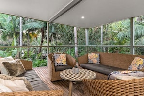 A room with a large glass window, wicker furniture, and a view of tropical foliage.