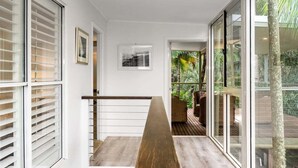 A staircase with a wooden handrail, white walls, and large glass doors leading to an outdoor area with greenery.