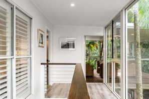 A staircase with a wooden handrail, white walls, and large glass doors leading to an outdoor area with greenery.