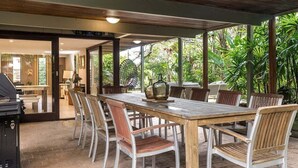 An outdoor dining area with a wooden table and chairs, surrounded by lush greenery.