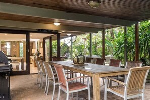 An outdoor dining area with a wooden table and chairs, surrounded by lush greenery.