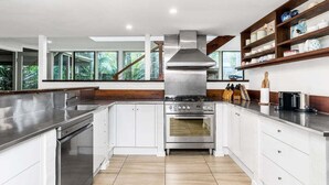 A modern kitchen with white cabinetry, stainless steel appliances, and a large window overlooking greenery.