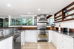 A modern kitchen with white cabinetry, stainless steel appliances, and a large window overlooking greenery.