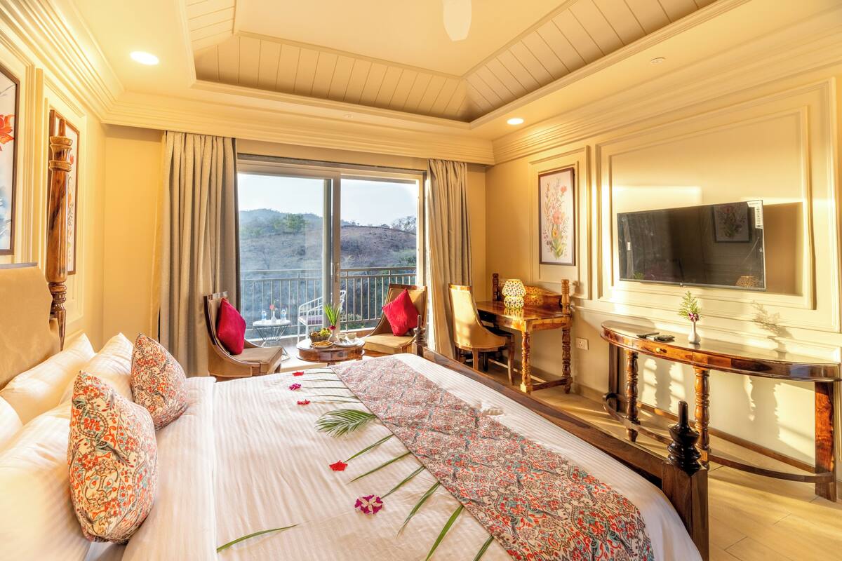 A hotel room with a large bed, a desk, a chair, a TV, and a balcony with a view.