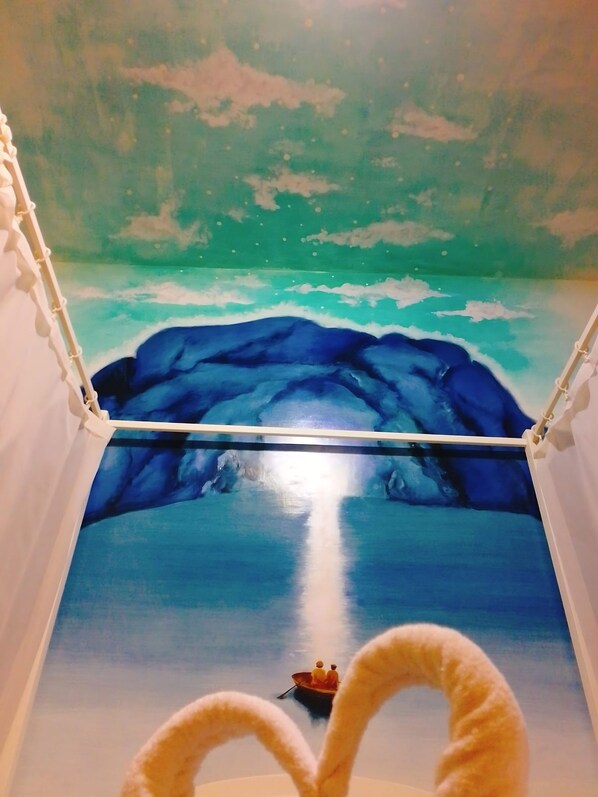 Una habitación con un mural de un mar tranquilo y un barco con dos figuras.