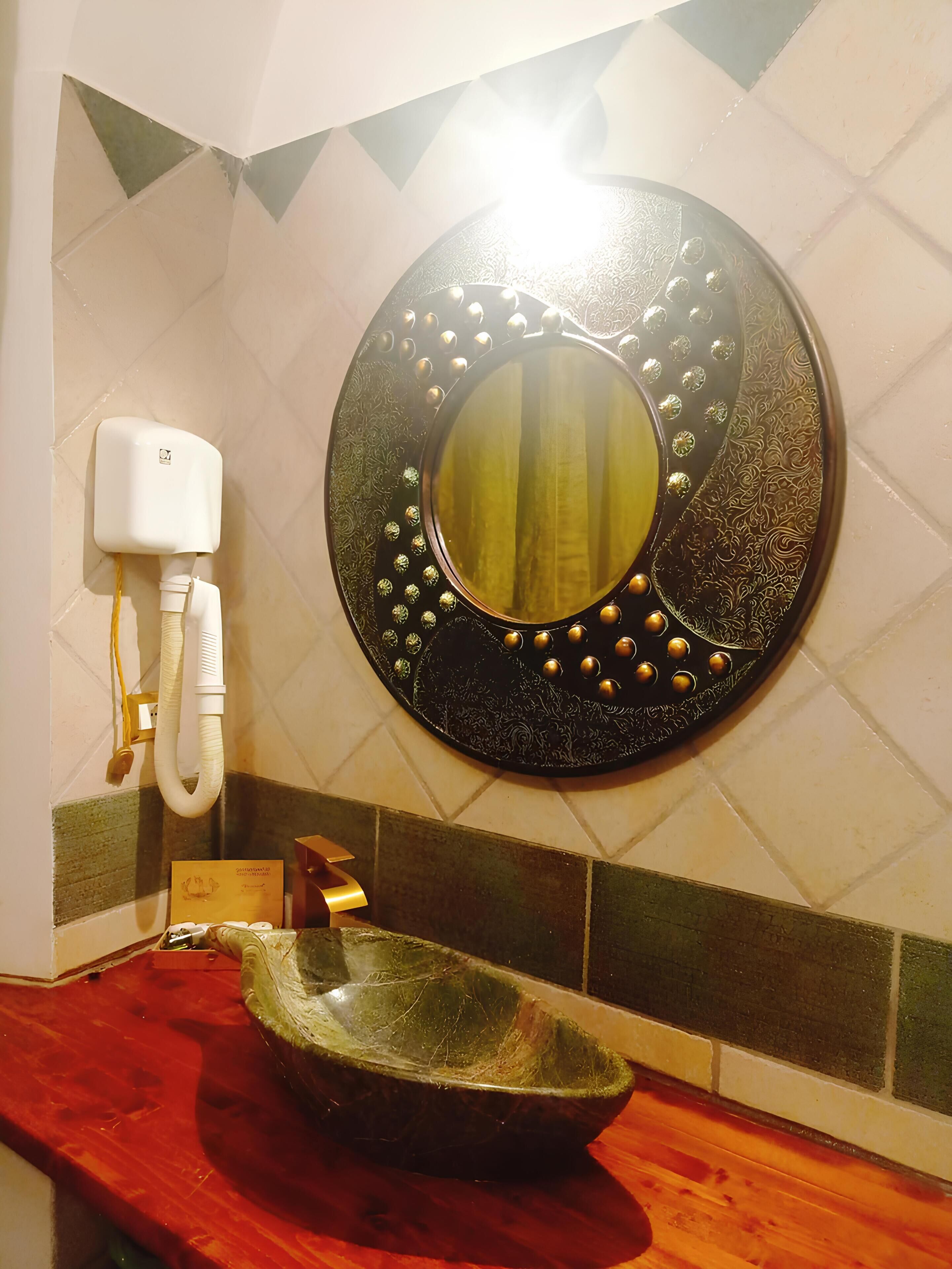 A bathroom with a round mirror, a hand soap dispenser, and a wooden sink.