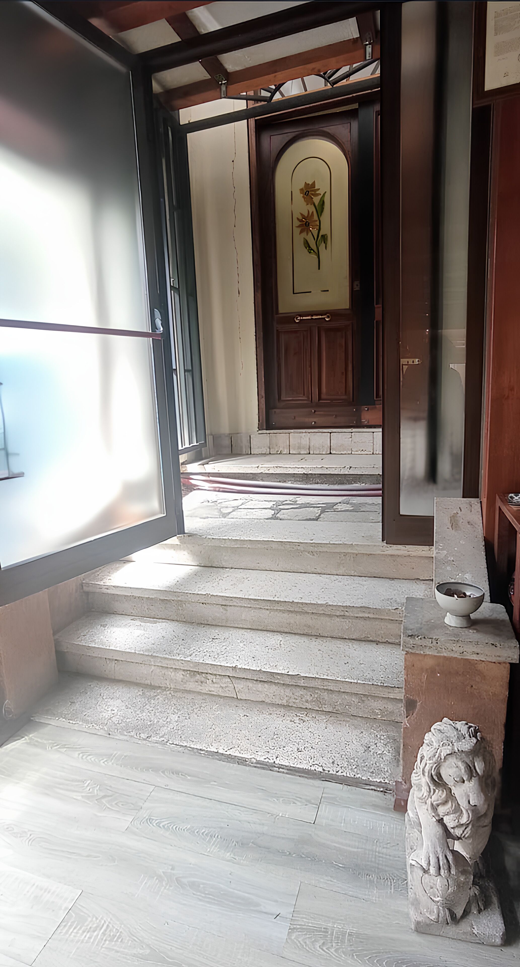 A staircase leading to a wooden door with a floral design, a stone statue, and a bowl on a ledge.