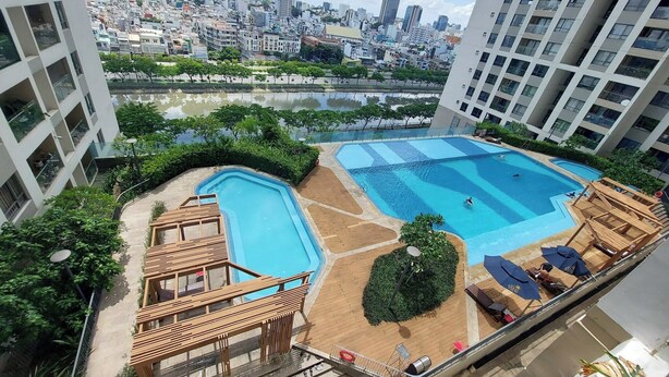 A rooftop pool area with two swimming pools, surrounded by greenery and overlooking a cityscape. - Gold View Quan 4 Aparment (Ho Chi Minh City)