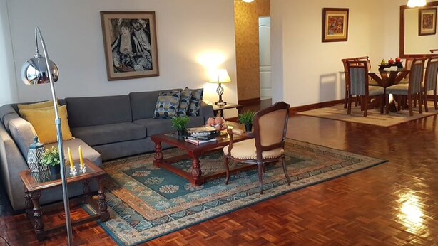 A living room with a sofa, coffee table, and armchairs, a dining area with a table and chairs, and a large painting on the wall. - Aparts4Days 2 Bedroom Apart San Isidro (Lima)