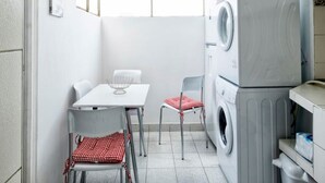 A compact laundry room with a table and two chairs, a washing machine, and a drying rack. - Aparts4Days 2 Bedroom Apart San Isidro (Lima)