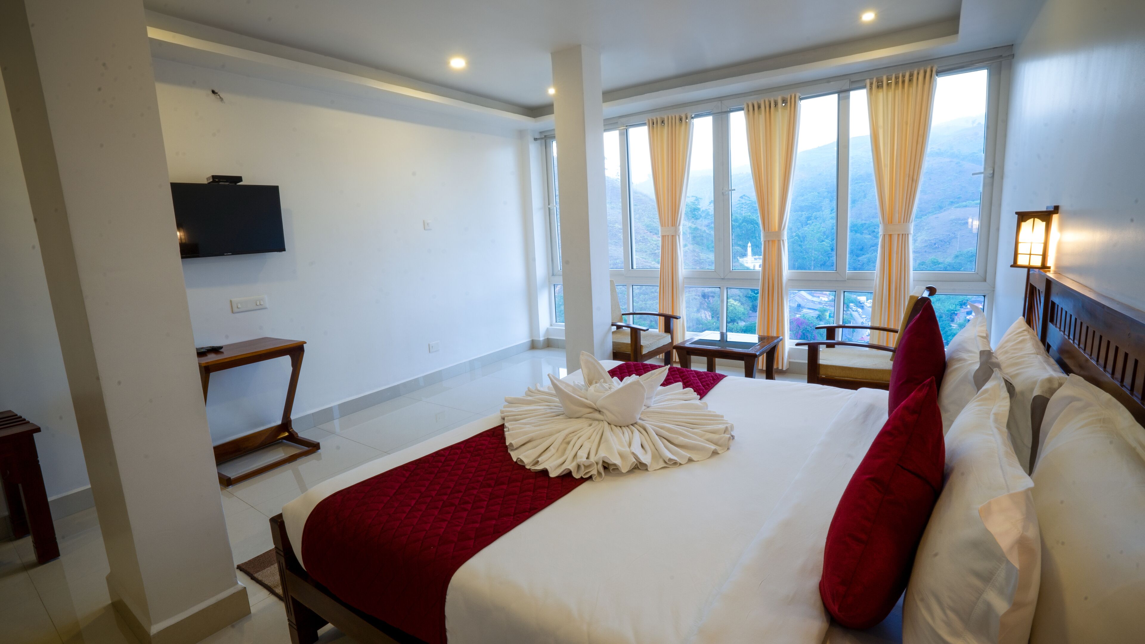 Une chambre d’hôtel avec un grand lit, une télévision, une vue sur les montagnes et une fenêtre avec des rideaux.